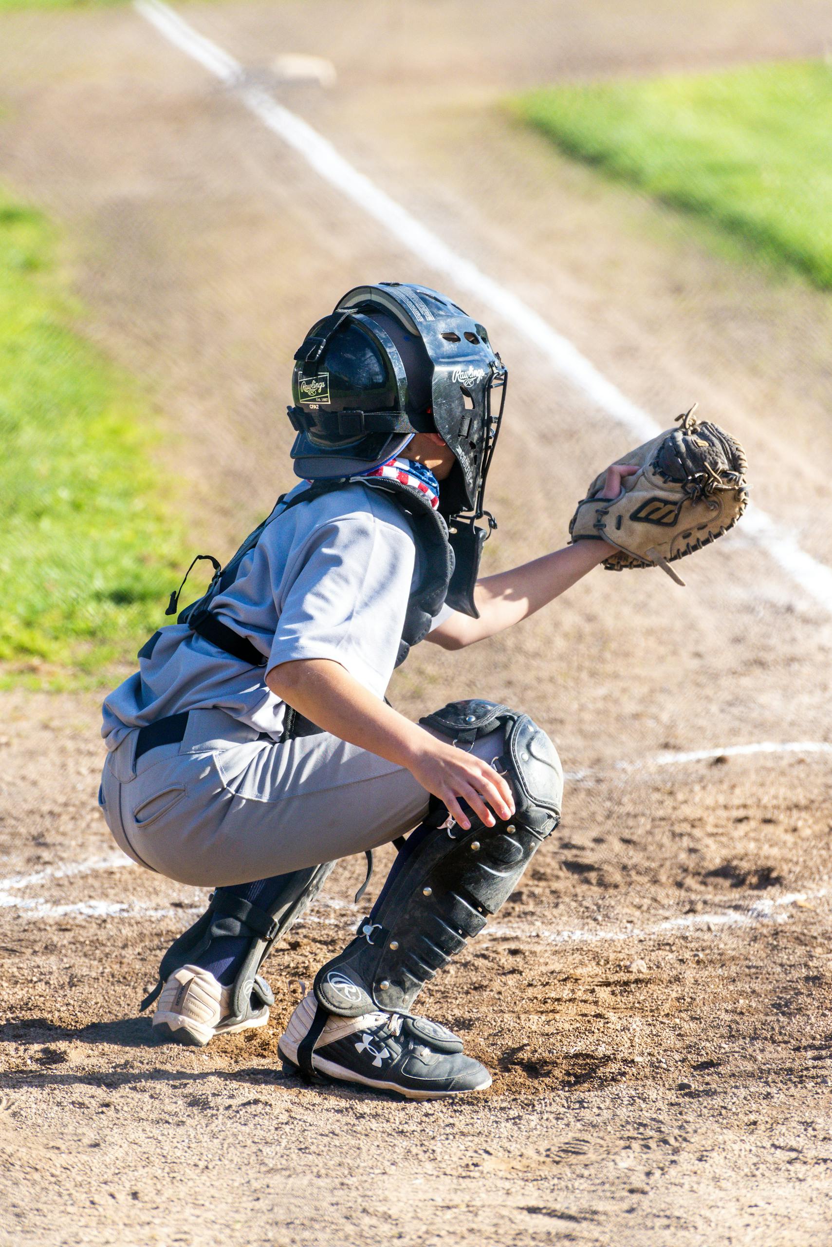 Rear view of a young catcher in full gear on a sunny day, ready to catch the ball during a baseball game.